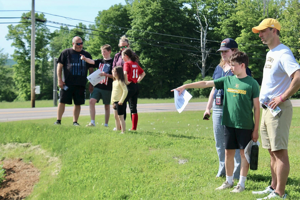 Students and adults point and gesture on a sunny grass school lawn
