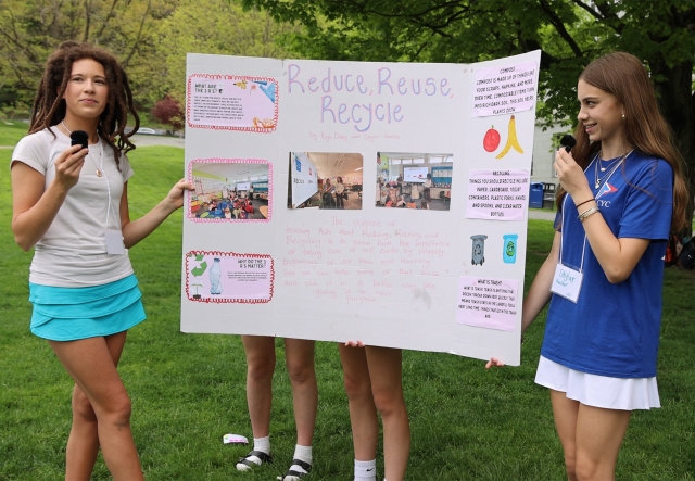 Two young people stand on either side of a posterboard titled Reduce Reuse Recycle