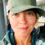 Woman in green ball cap with blonde hair smiles at camera. 